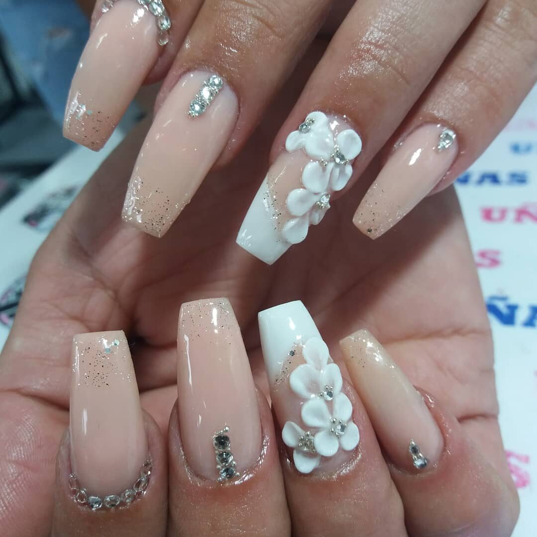 Uñas esculpidas nude con glitter, pedrería y flores blancas en relieve