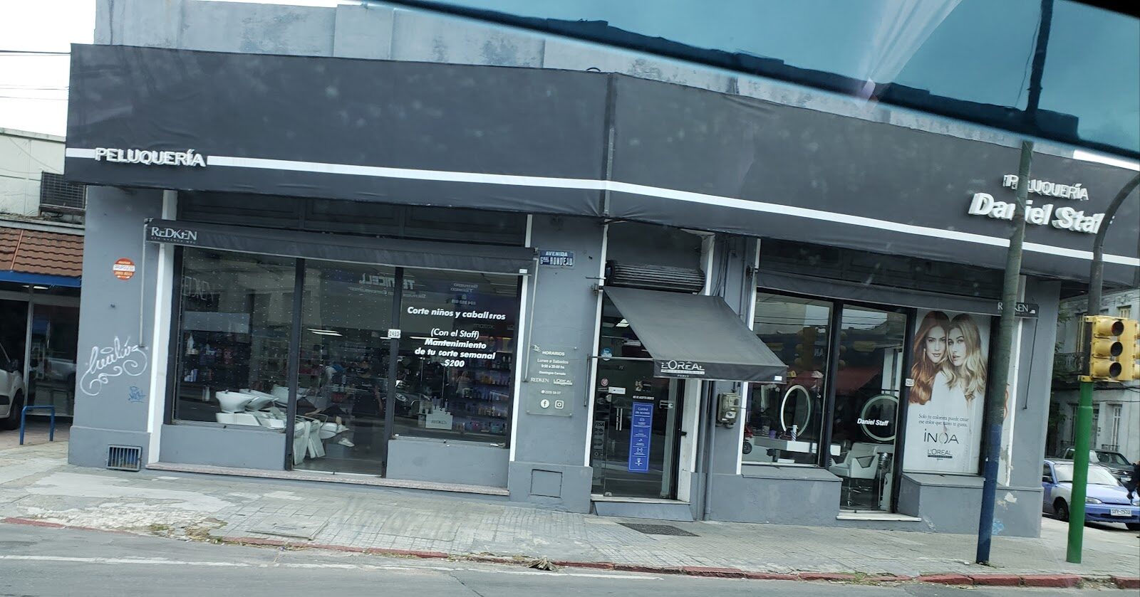 La fachada de la esquina: marquesina negra que dice Peluquería Daniel Staff, con el aviso pintado en la vidriera