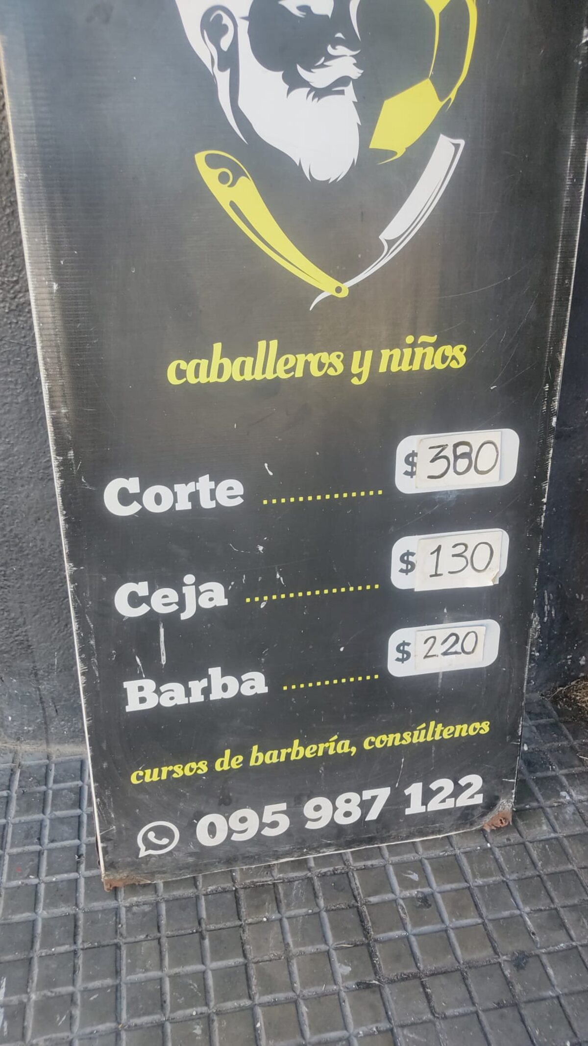 La pizarra de la vereda: corte $380, ceja $130, barba $220, cursos de barbería y el WhatsApp 095 987 122.