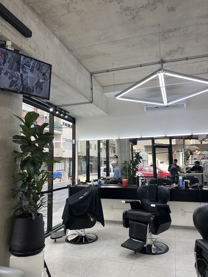 Interior de GOAT Barbería: techo de hormigón visto, luminaria geométrica y sillones negros frente a la vidriera