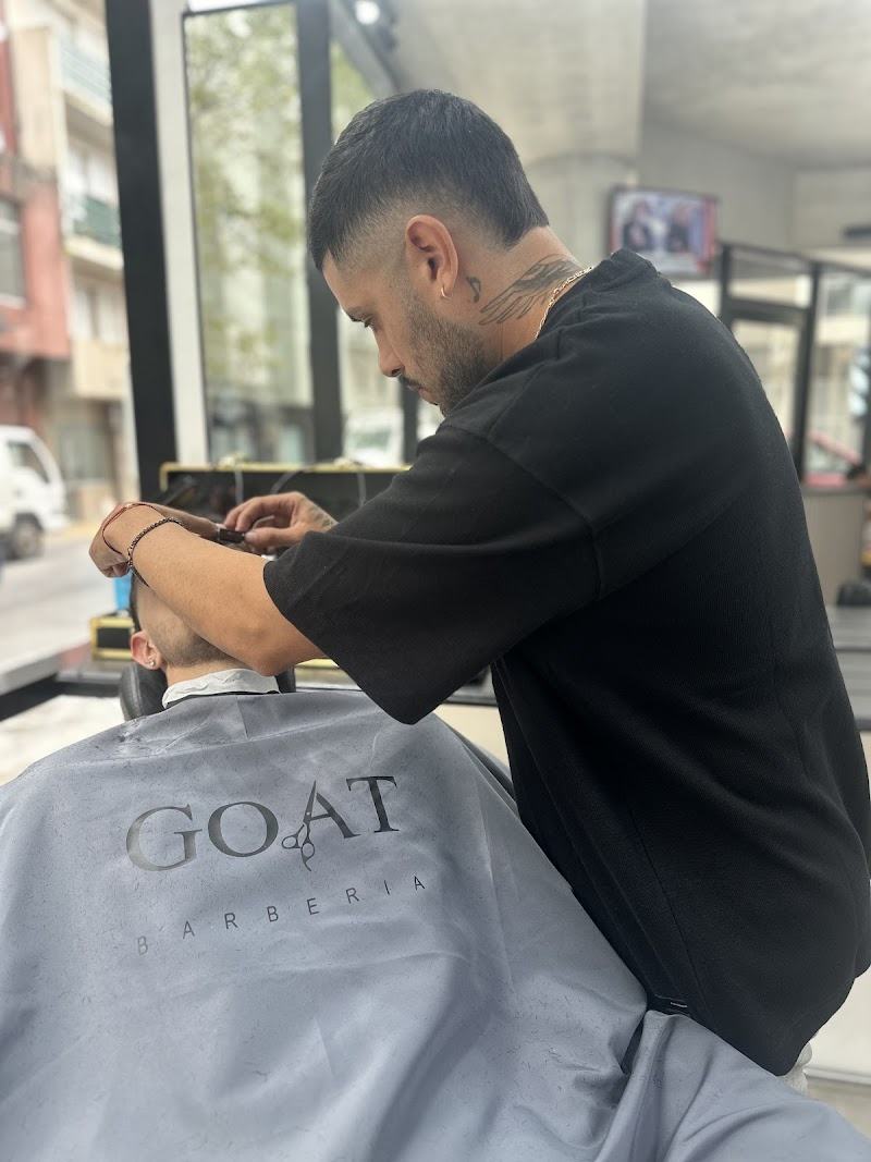 Barbero de GOAT trabajando sobre un cliente con la capa gris bordada de la barbería