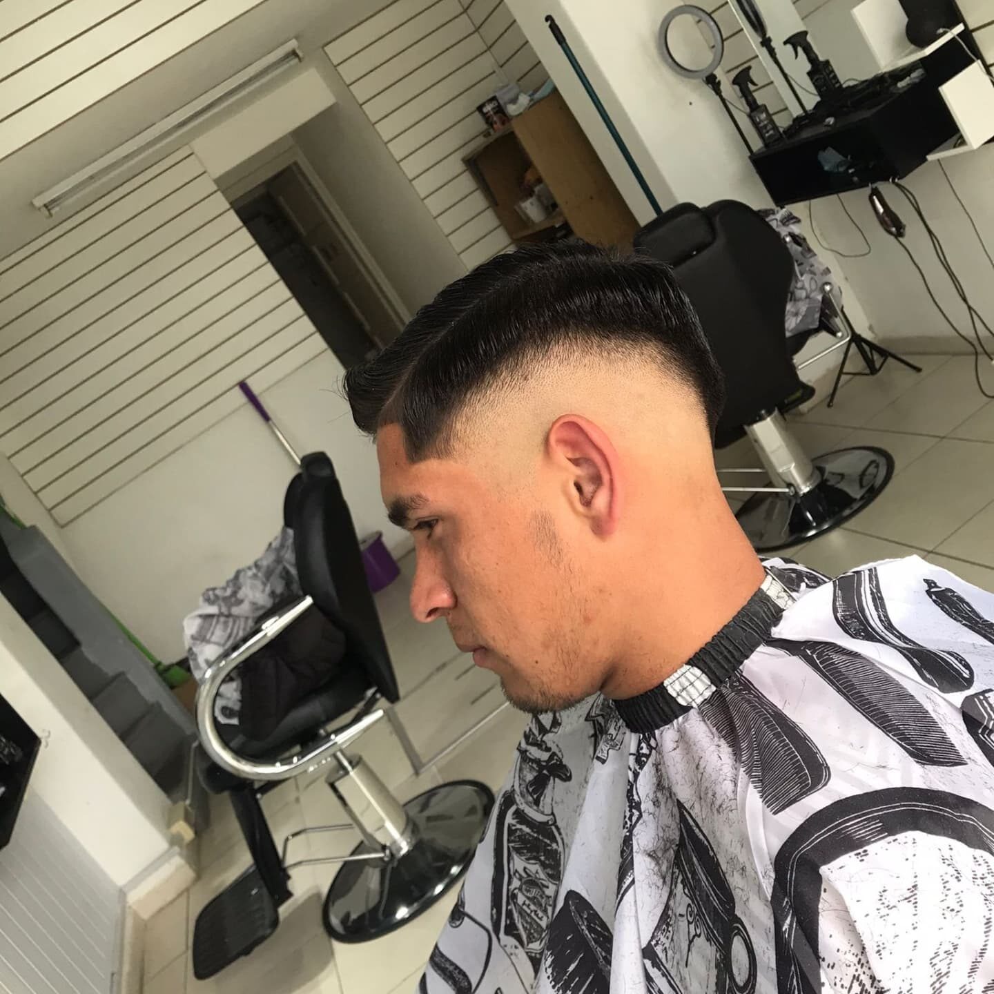 Corte terminado: fade alto a los costados y pelo peinado al costado con raya marcada a navaja.
