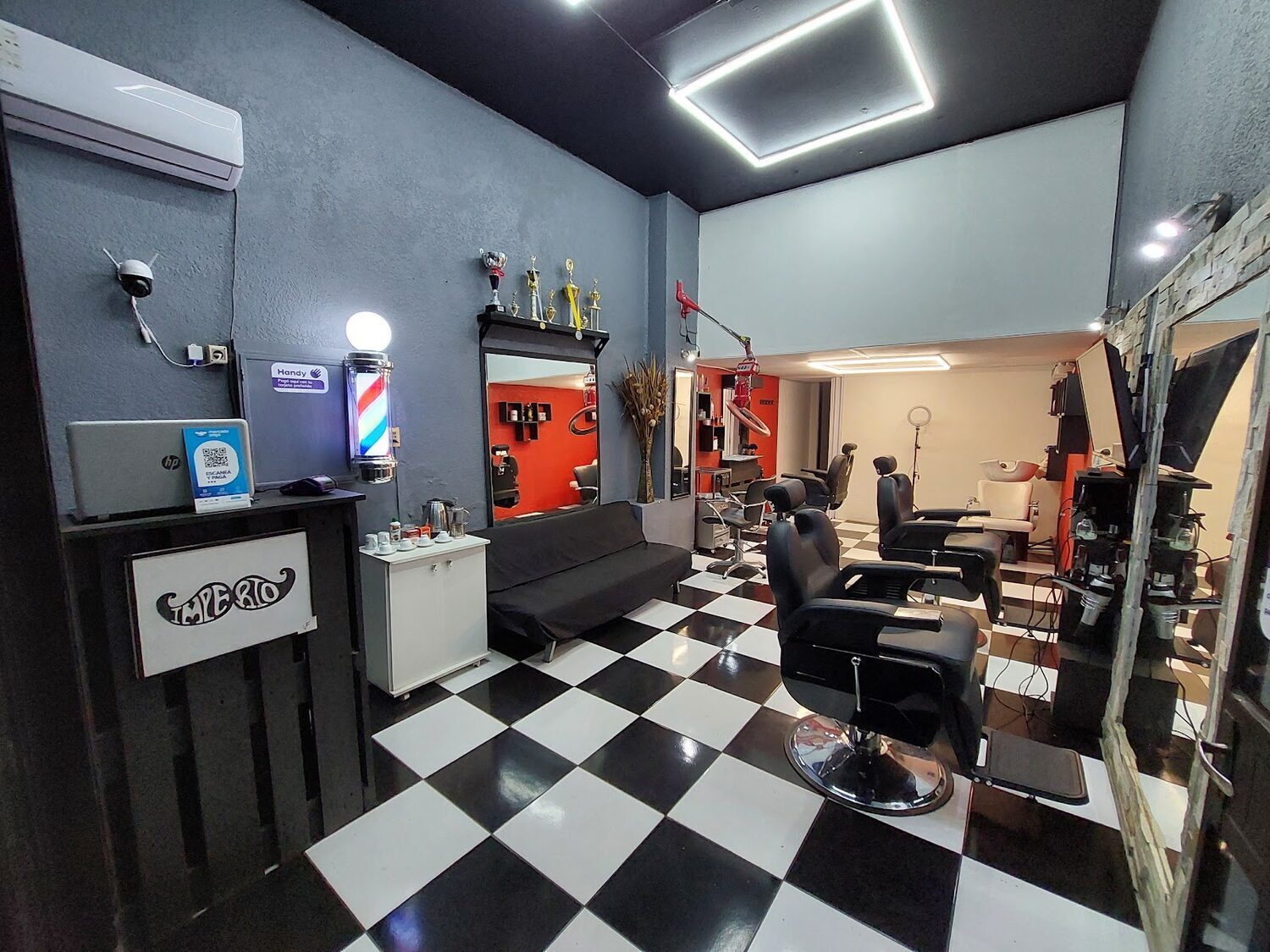 Salón de Imperio Barbershop: piso de damero blanco y negro, sillones de barbero, barber pole encendido y pared del fondo en rojo