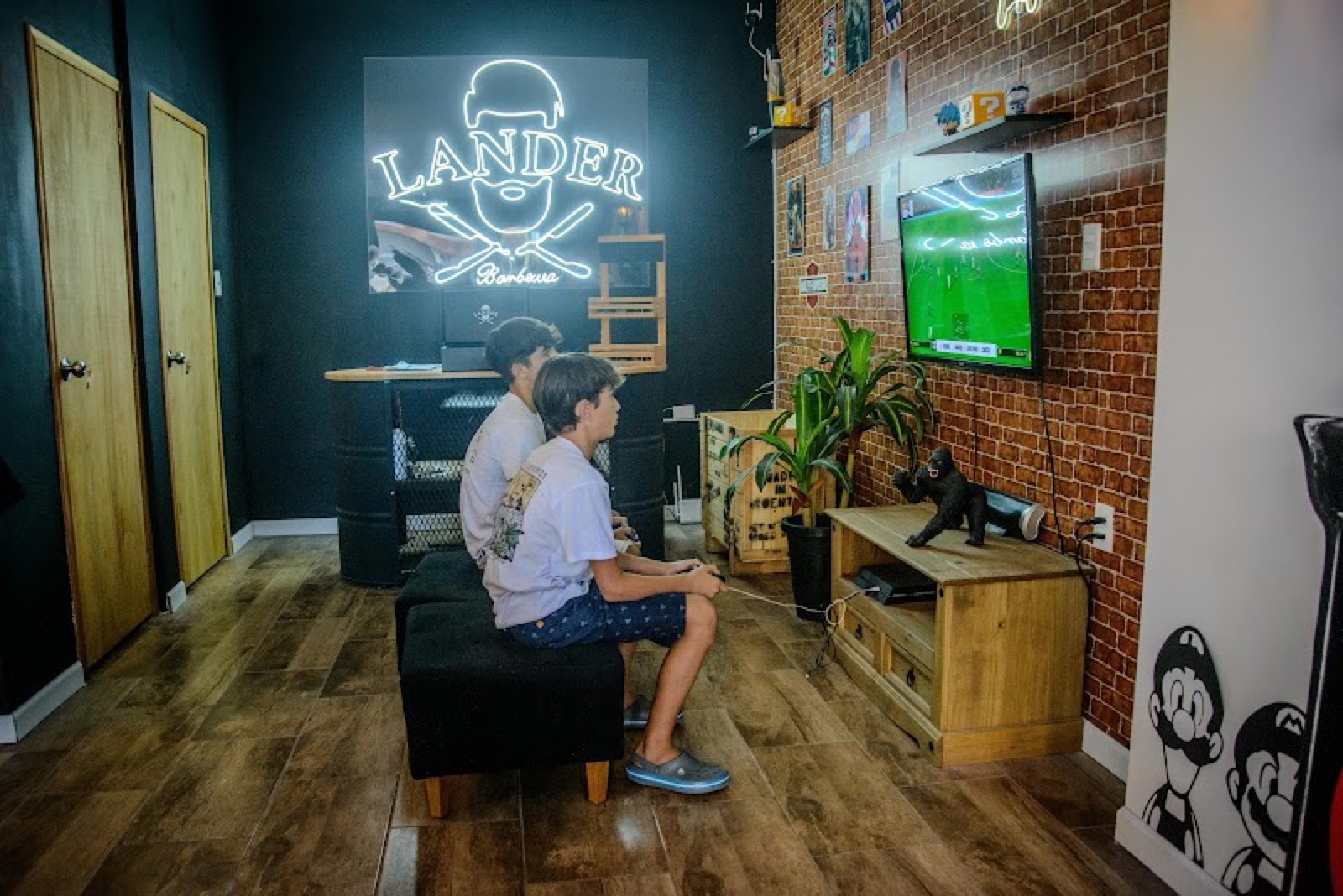 La sala de espera de Lander, con el cartel de neón y dos gurises jugando a la PlayStation.