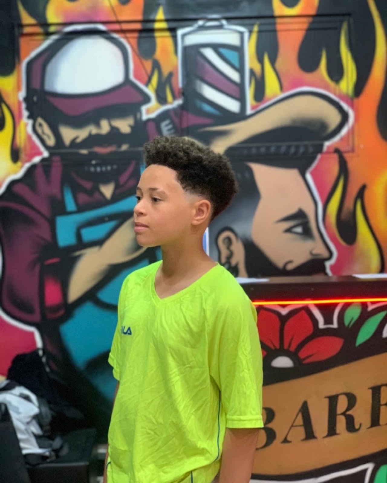Un cliente joven con el corte recién terminado, delante del mural del local.