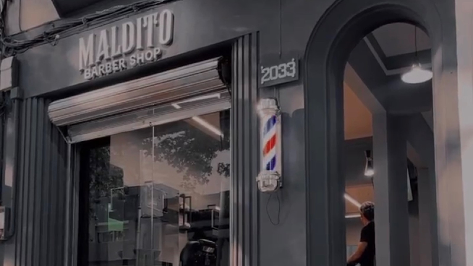 Fachada negra de Maldito Barber Shop sobre Constituyente: el cartel, el número 2033 y el barber pole junto a la puerta.