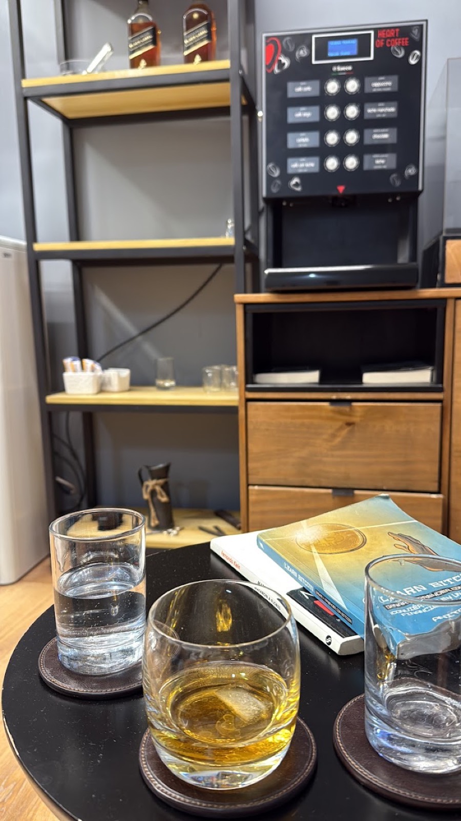 Mesa con vasos servidos frente a la cafetera y la estantería de la barbería.
