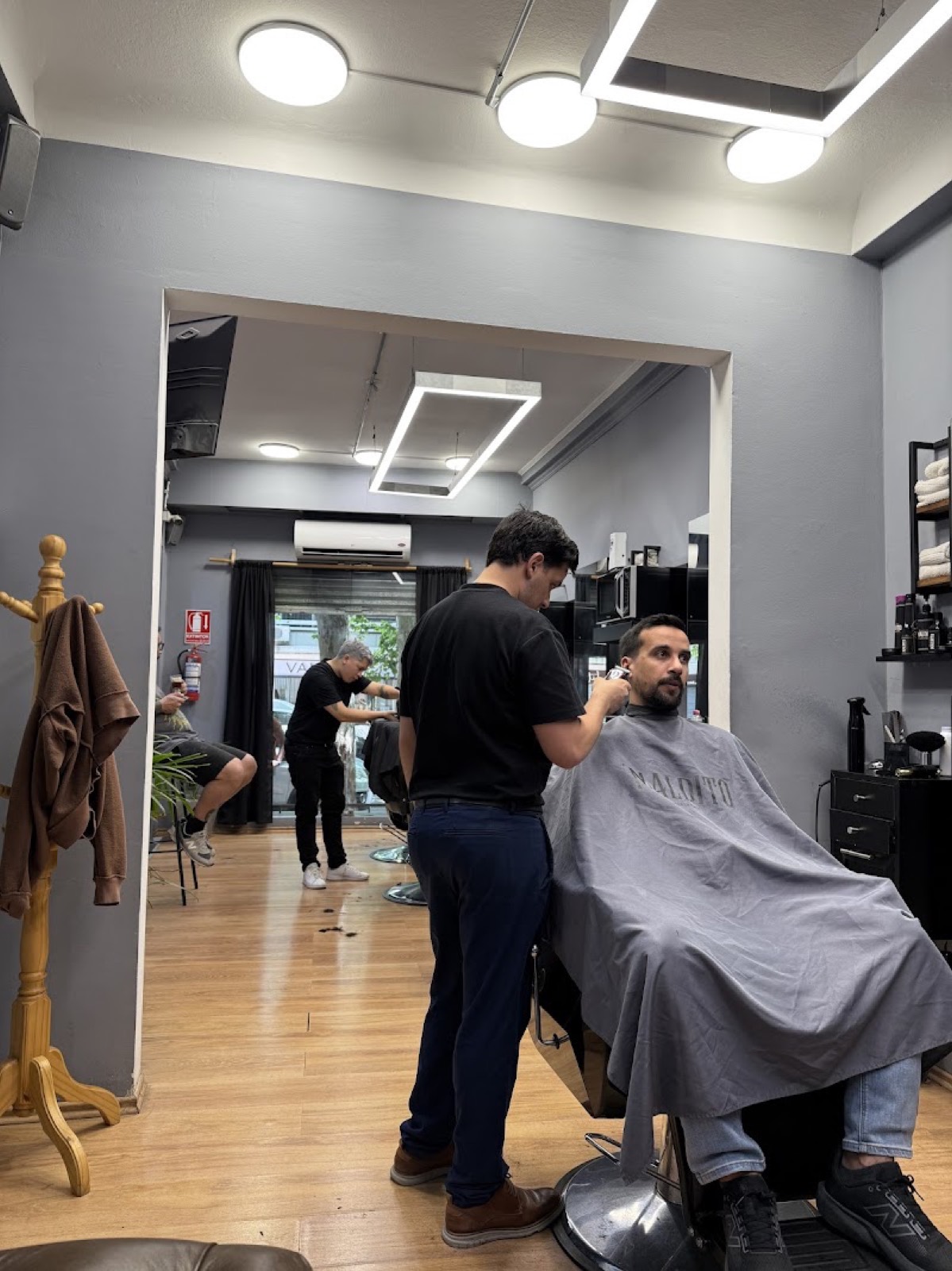Un barbero de Maldito perfilando a un cliente en la silla, con el salón al fondo.