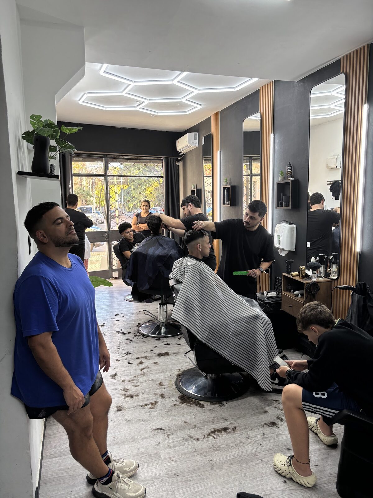 Dos barberos trabajando al mismo tiempo, con clientes esperando