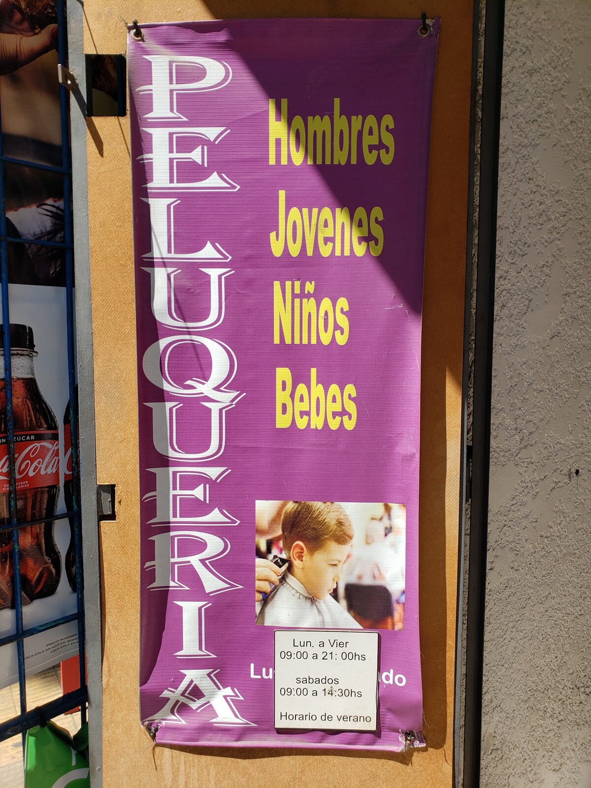 El banner violeta colgado en la puerta: «PELUQUERIA — Hombres, Jóvenes, Niños, Bebés».