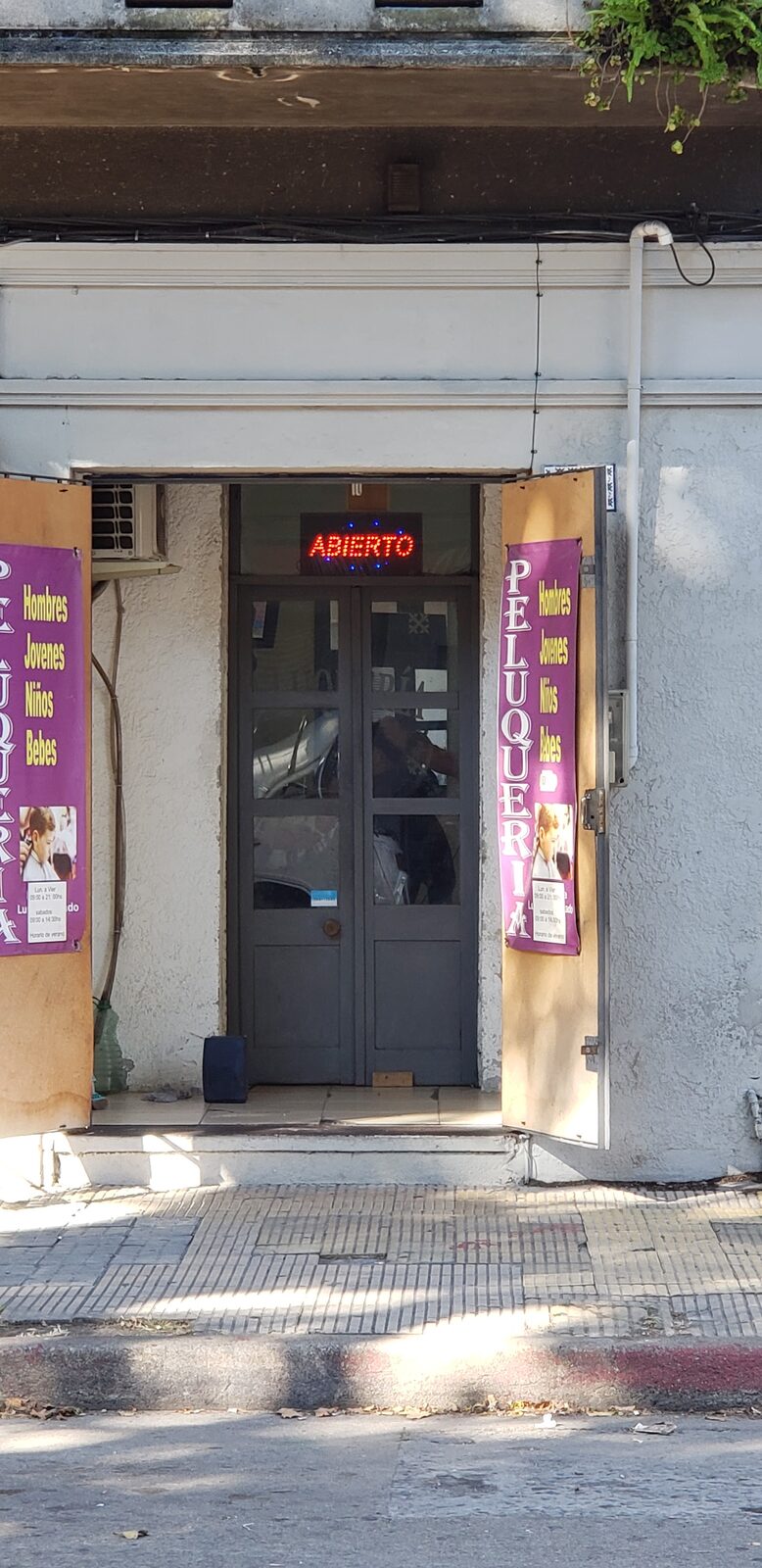 La puerta doble del local abierta de día, con el cartel de neón ABIERTO adentro.