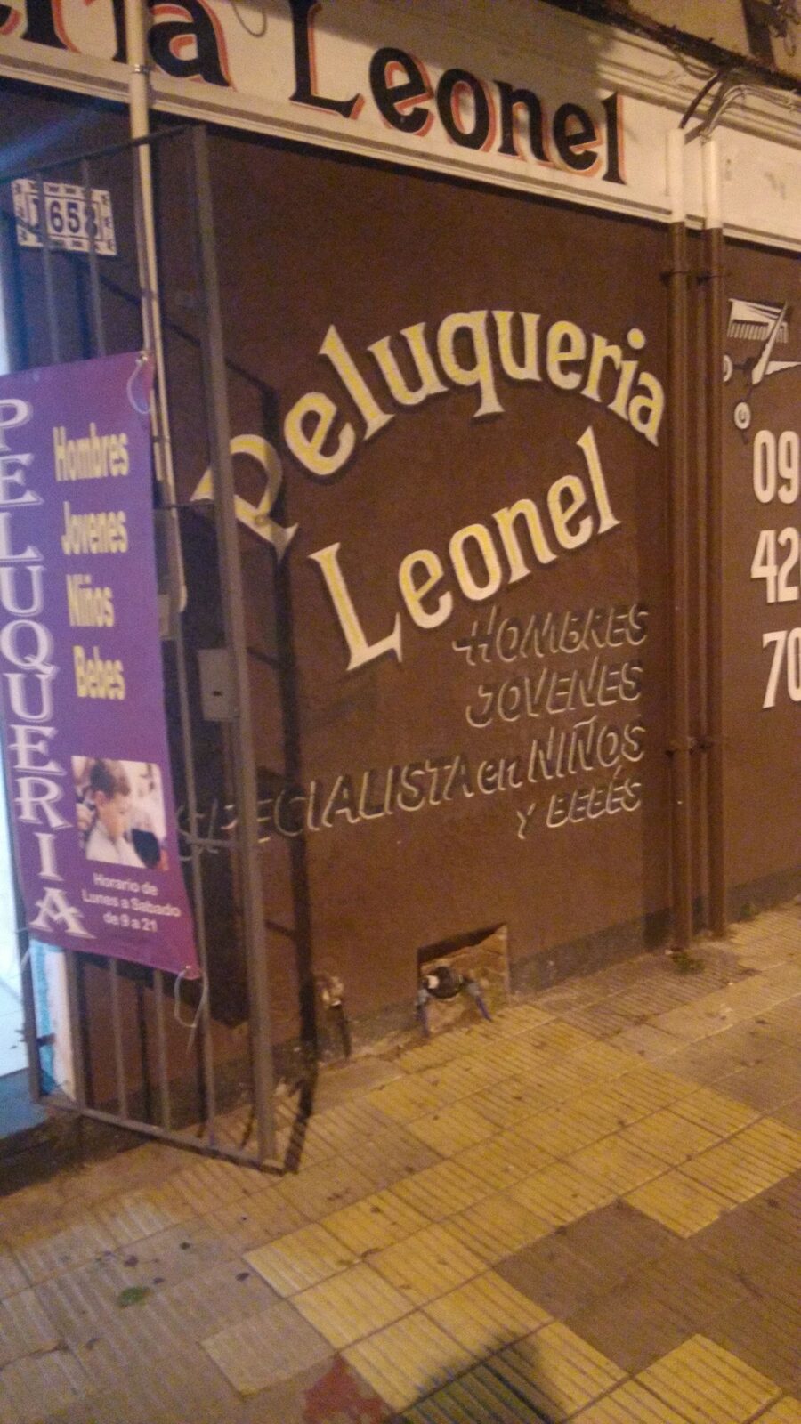 El frente del local de noche: pared marrón con «Peluqueria Leonel» pintado a mano en letras crema.