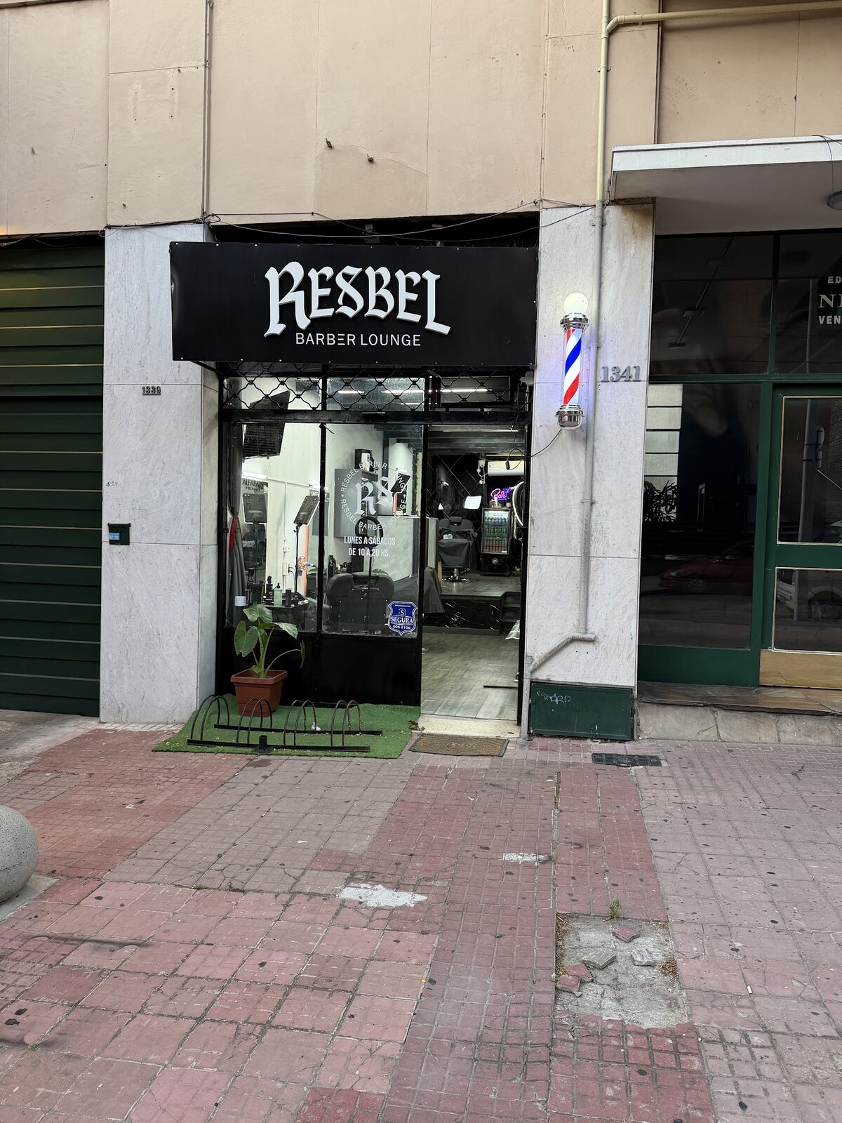 La fachada de Resbel Barber Lounge en Venezuela 1341: marquesina negra con el nombre en gótica, poste de barbero encendido y reja de rombos