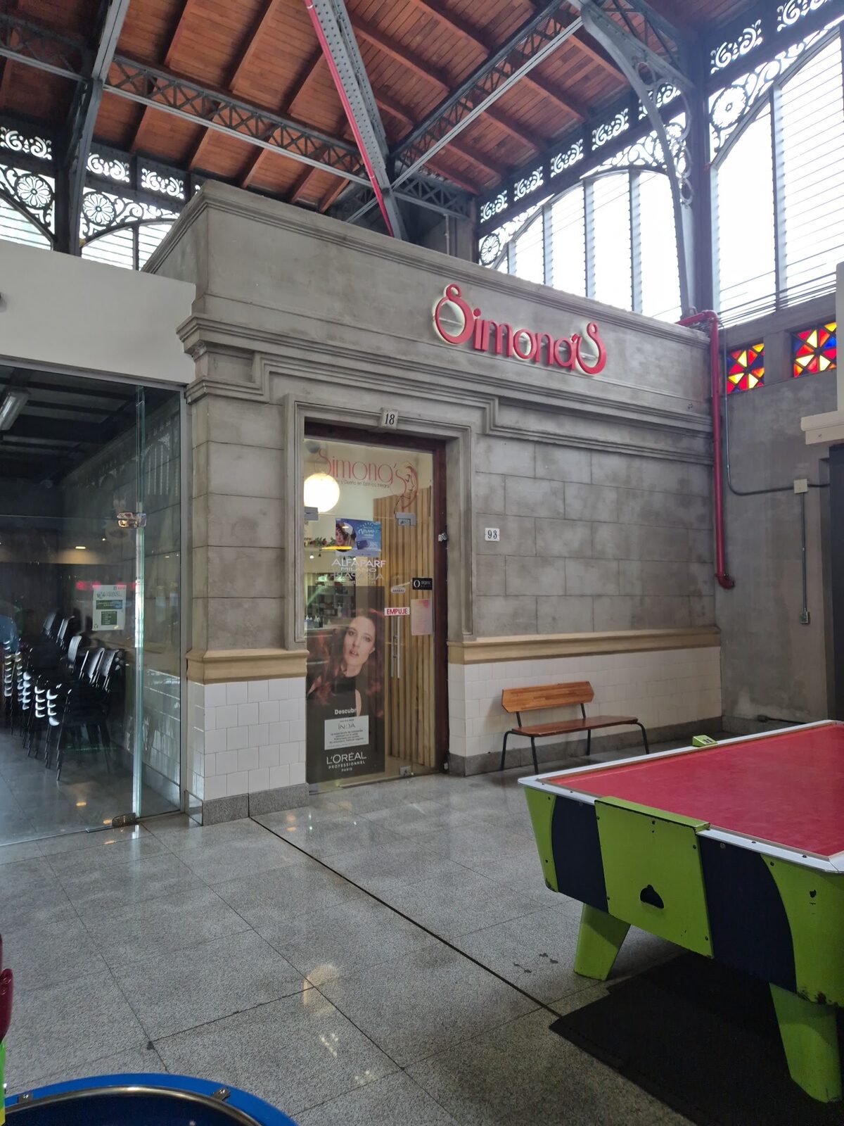 La entrada de Simona's adentro del Mercado Agrícola: cartel rojo corpóreo sobre la pared de piedra, bajo las cerchas de hierro y el techo de madera