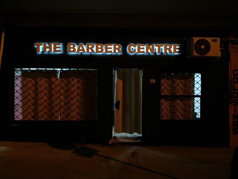 El cartel luminoso de The Barber Centre encendido de noche sobre la vereda.