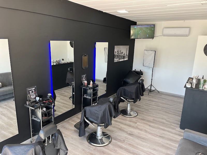 Interior del local: pared negra, espejos con luz, sillones de barbero y televisor.