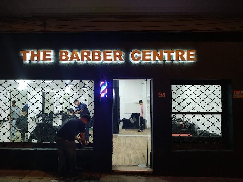 Frente de The Barber Centre de noche, con el cartel luminoso encendido y los barberos trabajando adentro.