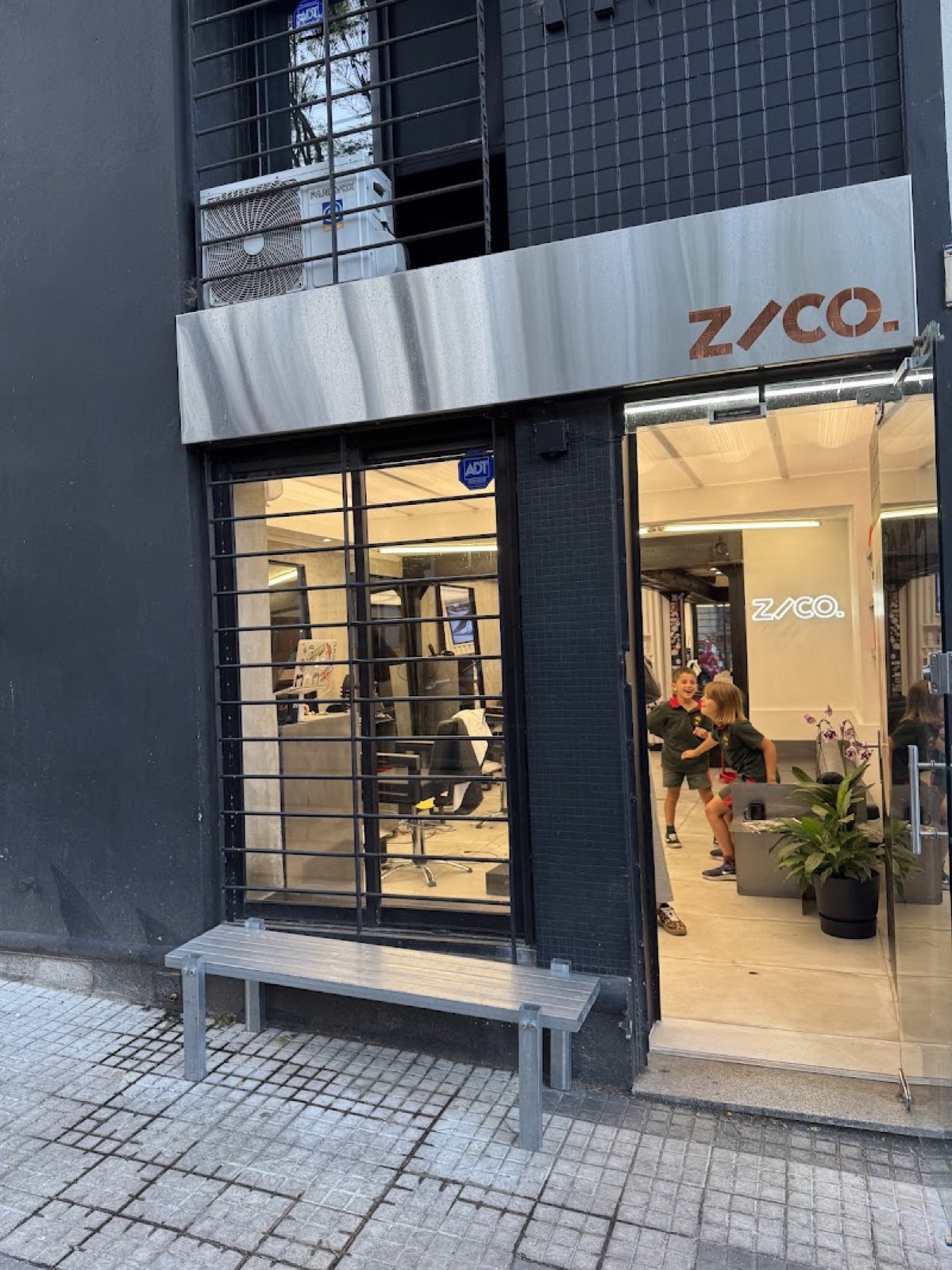 Frente de ZACO. en Charrúa 2247: cartel de acero con las letras de cobre, banco en la vereda y la puerta abierta.